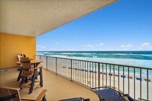 A balcony with a view of the ocean, wooden chairs, and a table.