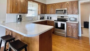 A kitchen with wooden cabinets, a central island with stools, stainless steel appliances, and a tiled backsplash. - The Bird House has at least one ‘bird’ in each room. How many can you find? (Kansas City)