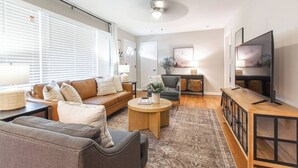 Ein modernes Wohnzimmer mit Sofa, Sessel, Couchtisch und Fernseher.