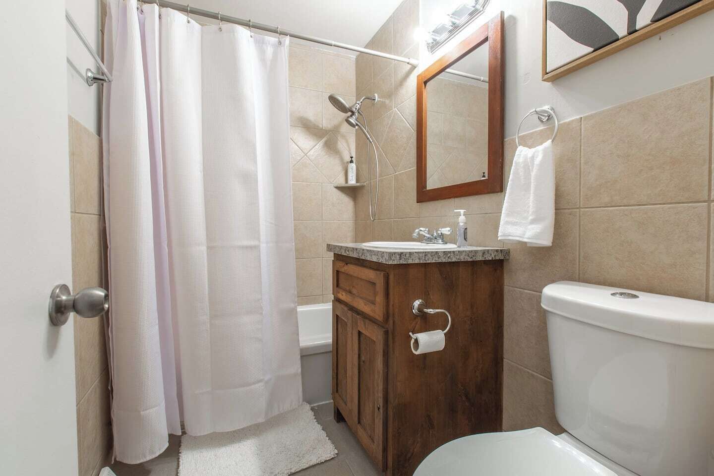 Een badkamer met douche, toilet, wastafel en een houten wastafelmeubel.