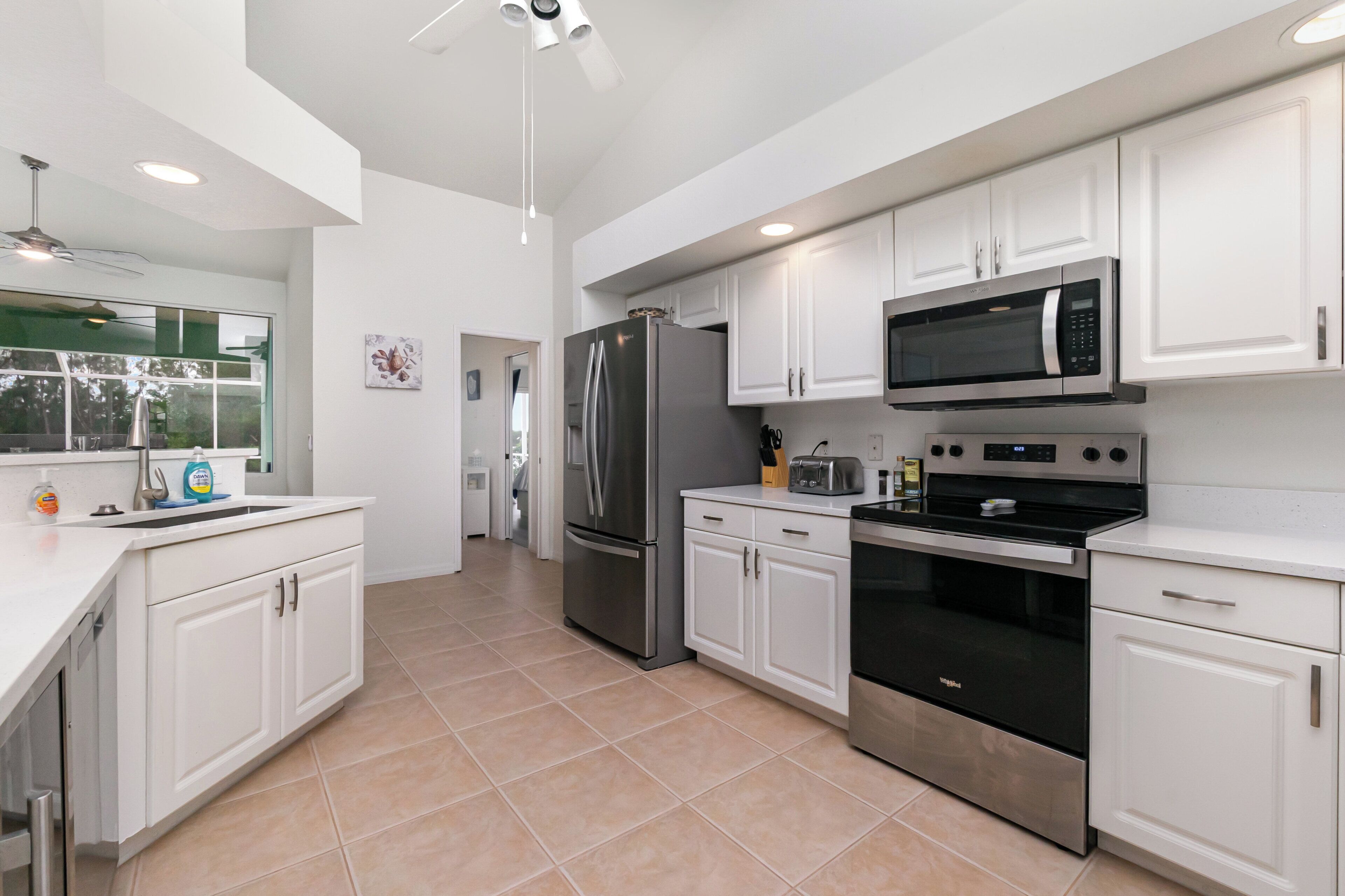 A modern kitchen with white cabinets, stainless steel appliances, and a large window.