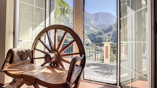 Et træbord og stole på en balkon med udsigt til bjerge og en by.