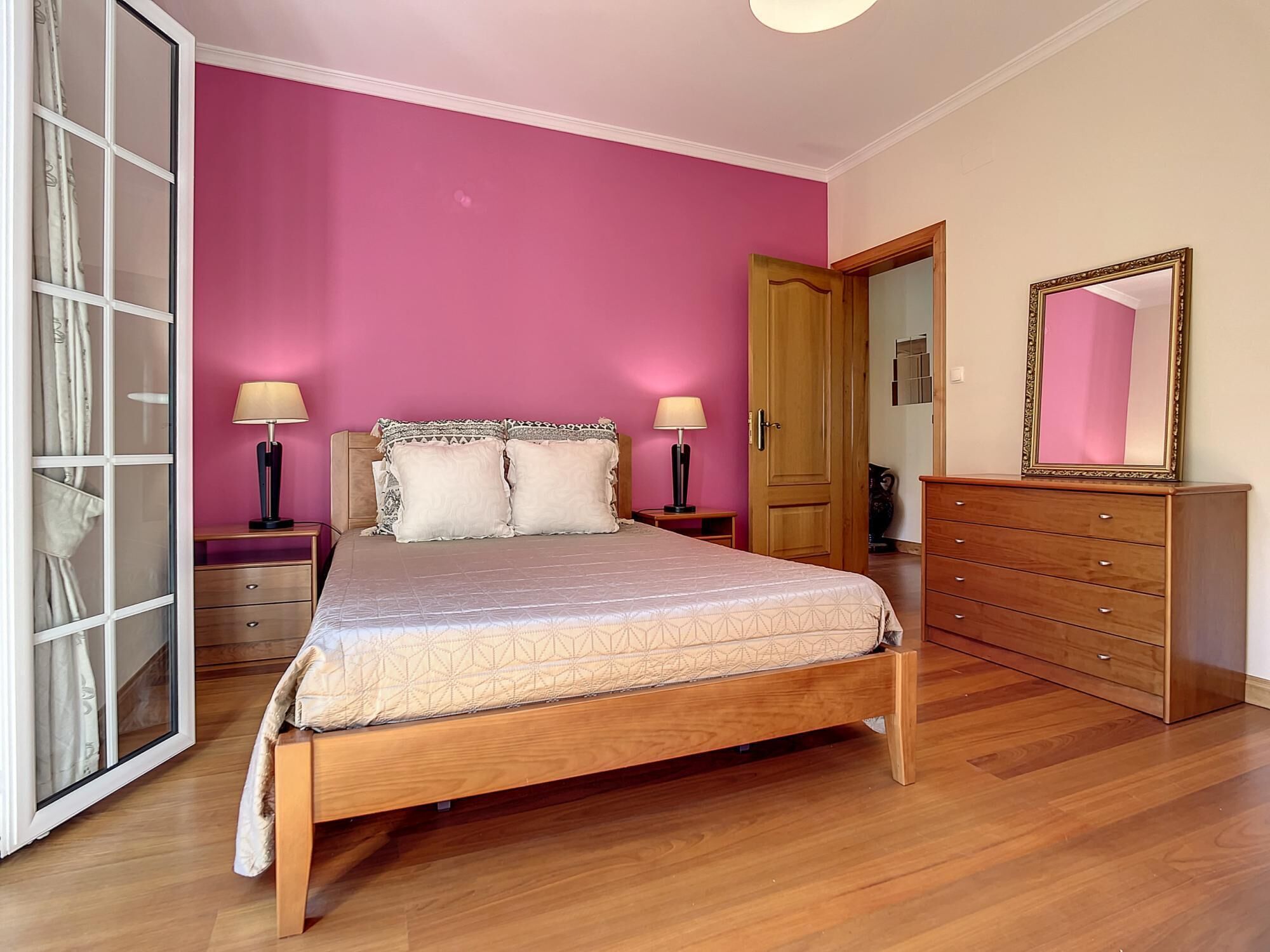 A bedroom with a bed, bedside tables, a dresser, a mirror, and a wardrobe.