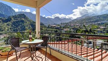 A balcony with a table and chairs, overlooking a mountainous landscape with houses.