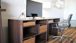 A modern office space with a large flat-screen TV, a wooden desk with multiple drawers, a metal office chair, and a striped carpet. - Super 8 by Wyndham Wells (Wells)