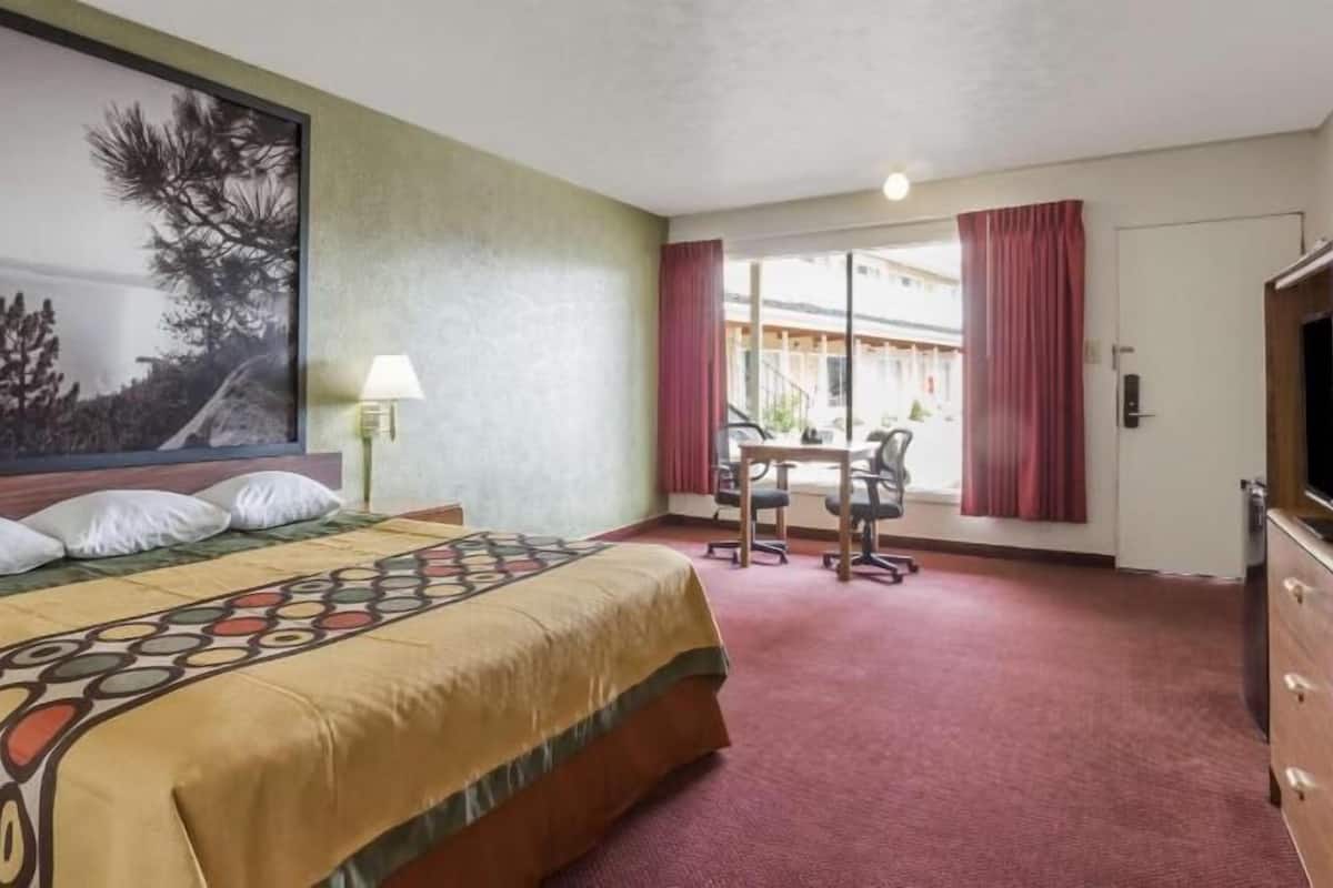 A hotel room with a bed, a desk, a chair, a TV, and a large window with curtains.