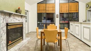 A dining area with a marble fireplace, a table with chairs, and a kitchen with large windows and bamboo blinds. - Super 8 by Wyndham Wells (Wells)