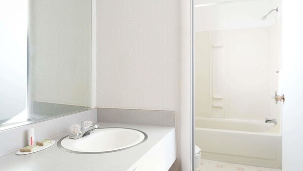 A bathroom with a white sink, a mirror, and a shower area. - Super 8 by Wyndham Wells (Wells)