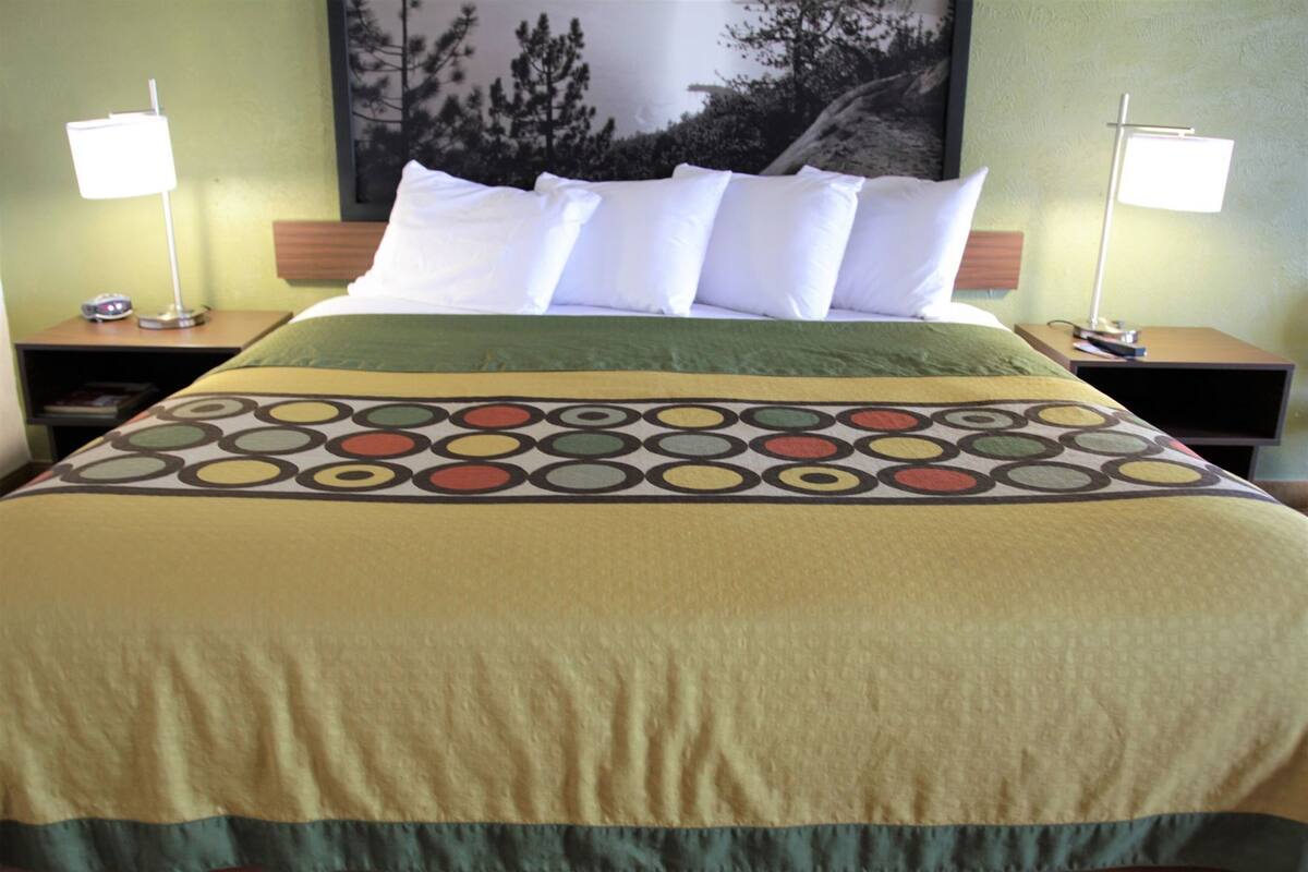 A hotel room with a bed, two nightstands, a lamp on each, and a large framed picture on the wall.