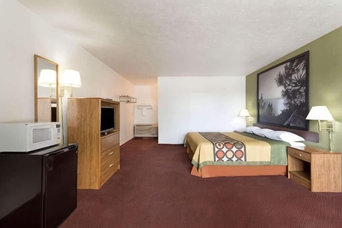 A hotel room with a bed, a TV, a desk, a lamp, a dresser, and a painting on the wall.