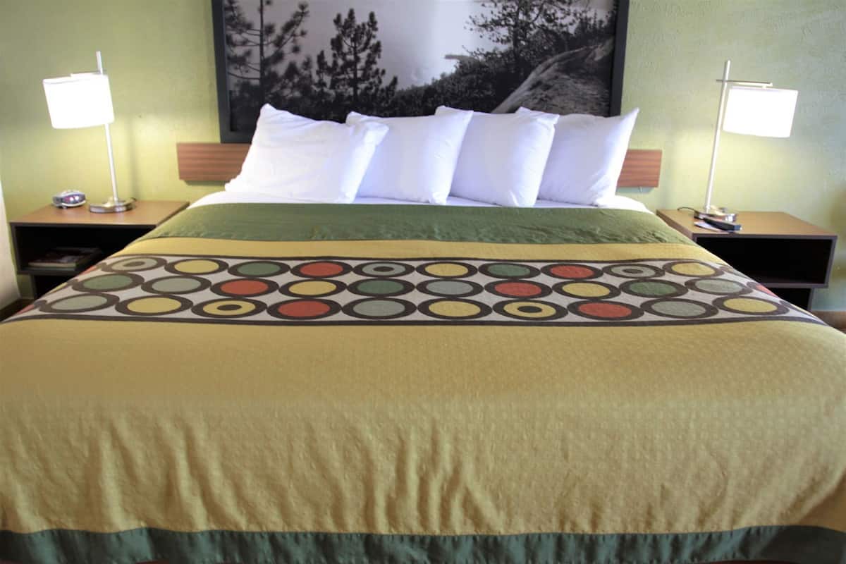 A hotel room with a bed, two nightstands, a lamp on each, and a large framed picture on the wall.