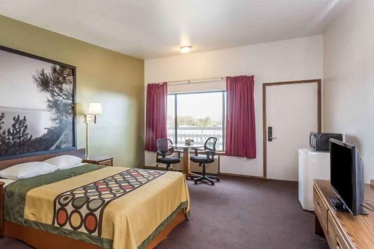 A hotel room with a bed, desk, chair, television, and a large window with curtains.
