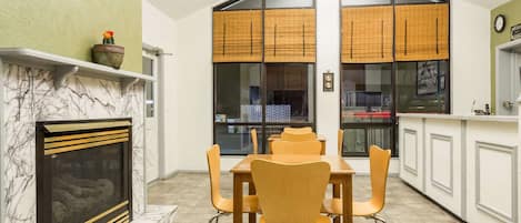 A dining area with a marble fireplace, wooden chairs, and a table.