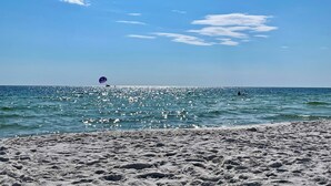Une plage avec un ciel dégagé, une mer calme et un parachute ascensionnel visible au loin.