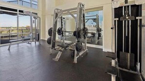 Une salle de sport équipée de matériel de musculation, dotée de grandes fenêtres et offrant une vue sur l’extérieur.