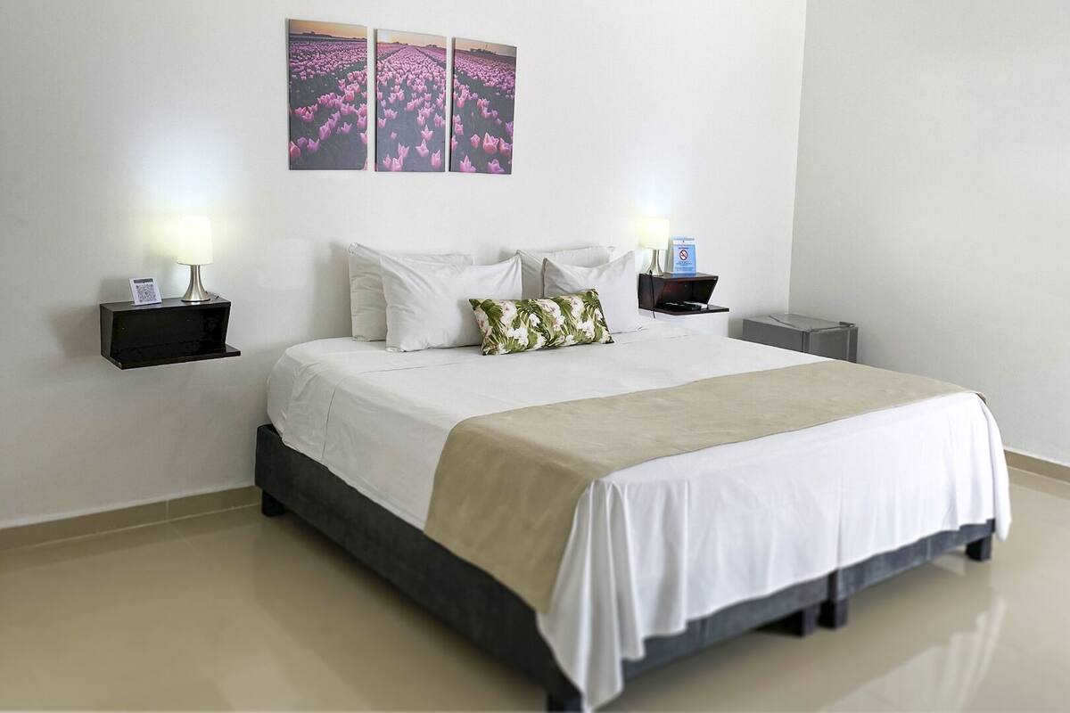 A neatly arranged hotel room with a bed, two bedside tables, a nightstand, and a wall-mounted light fixture.