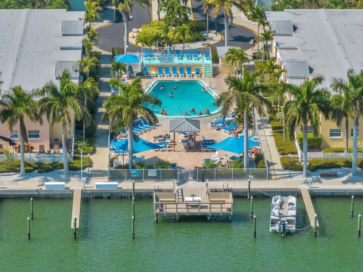 An aerial view of a resort with a central pool surrounded by lounge chairs and palm trees.