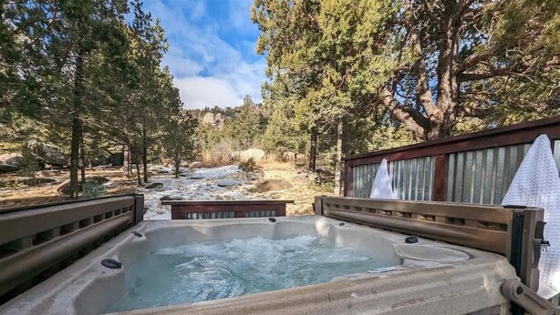 A hot tub surrounded by trees, with a wooden deck and a metal railing. - Mountain Zen (Alto)