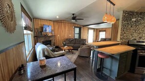 A modern kitchen with a bar area, a dining table, and a living area with a sofa and TV. - Mountain Zen (Alto)