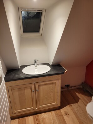 A small bathroom with a white sink, wooden cabinets, and a window above the sink.