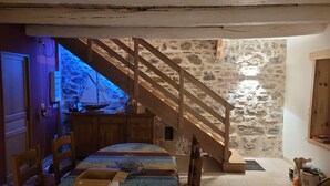 A rustic room with a wooden staircase, stone walls, a dining table with chairs, and a bed. - Forsythias (Messeix)