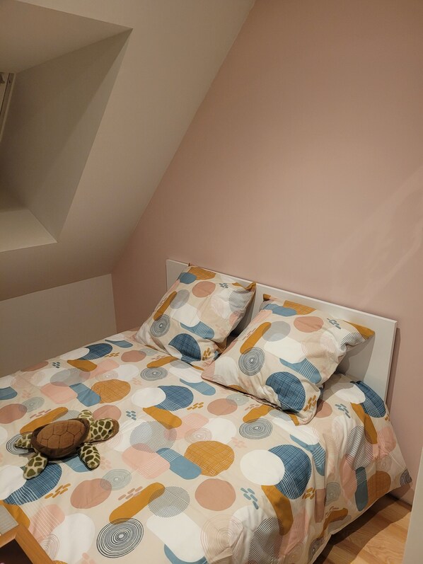 A bedroom with a sloped ceiling, a bed with a patterned bedspread, and a giraffe-shaped pillow.