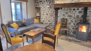 A cozy living room with a stone wall, a sofa, a wooden table, and a fireplace. - Forsythias (Messeix)