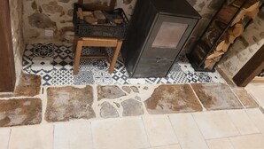 A rustic room with a stone wall, a wooden chair, a black cabinet, and a tiled floor. - Forsythias (Messeix)