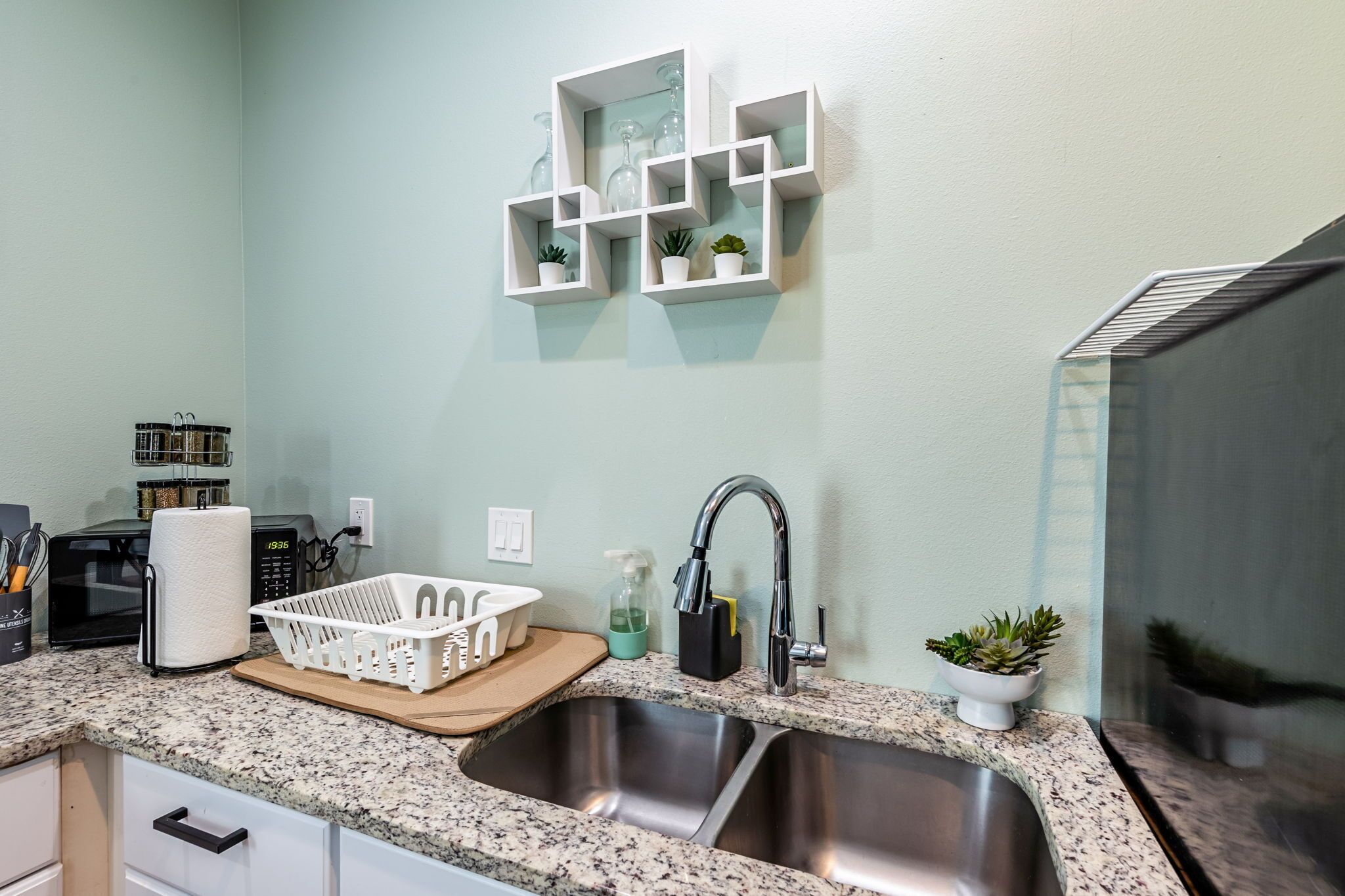 A kitchen with granite countertops, a stainless steel sink, a microwave, and a white basket on the counter.