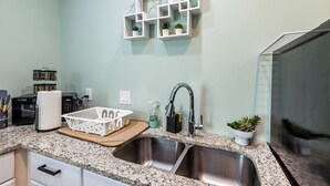 Une cuisine dotée de plans de travail en granit, d’un évier en acier inoxydable, d’un four à micro-ondes et d’un panier blanc posé sur le plan de travail.