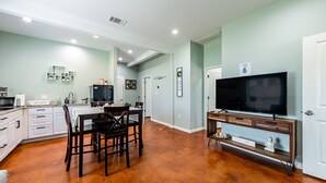Une cuisine spacieuse avec des meubles blancs, une table à manger avec des chaises, un téléviseur à écran plat posé sur un meuble en bois et un mur de couleur vert clair.