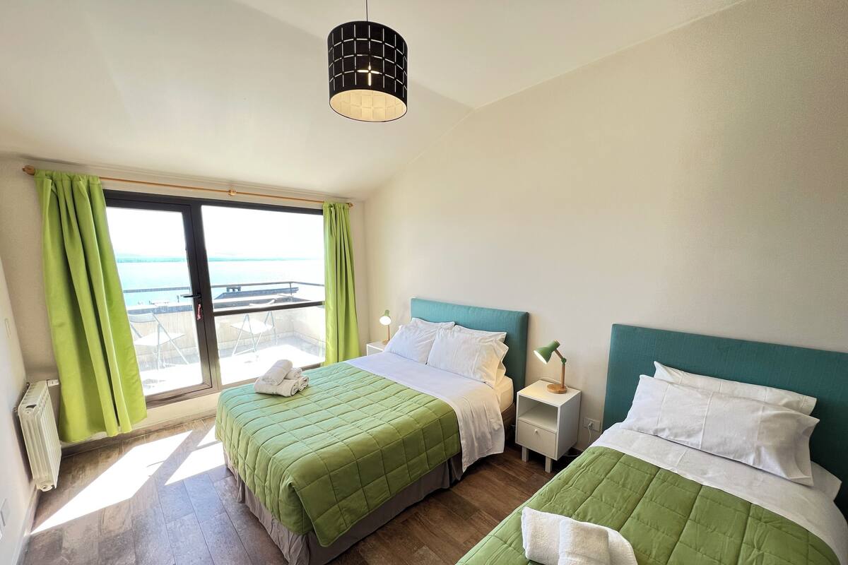 Habitació d'hotel amb dos llits, vista al mar, un balcó i una làmpada penjant.