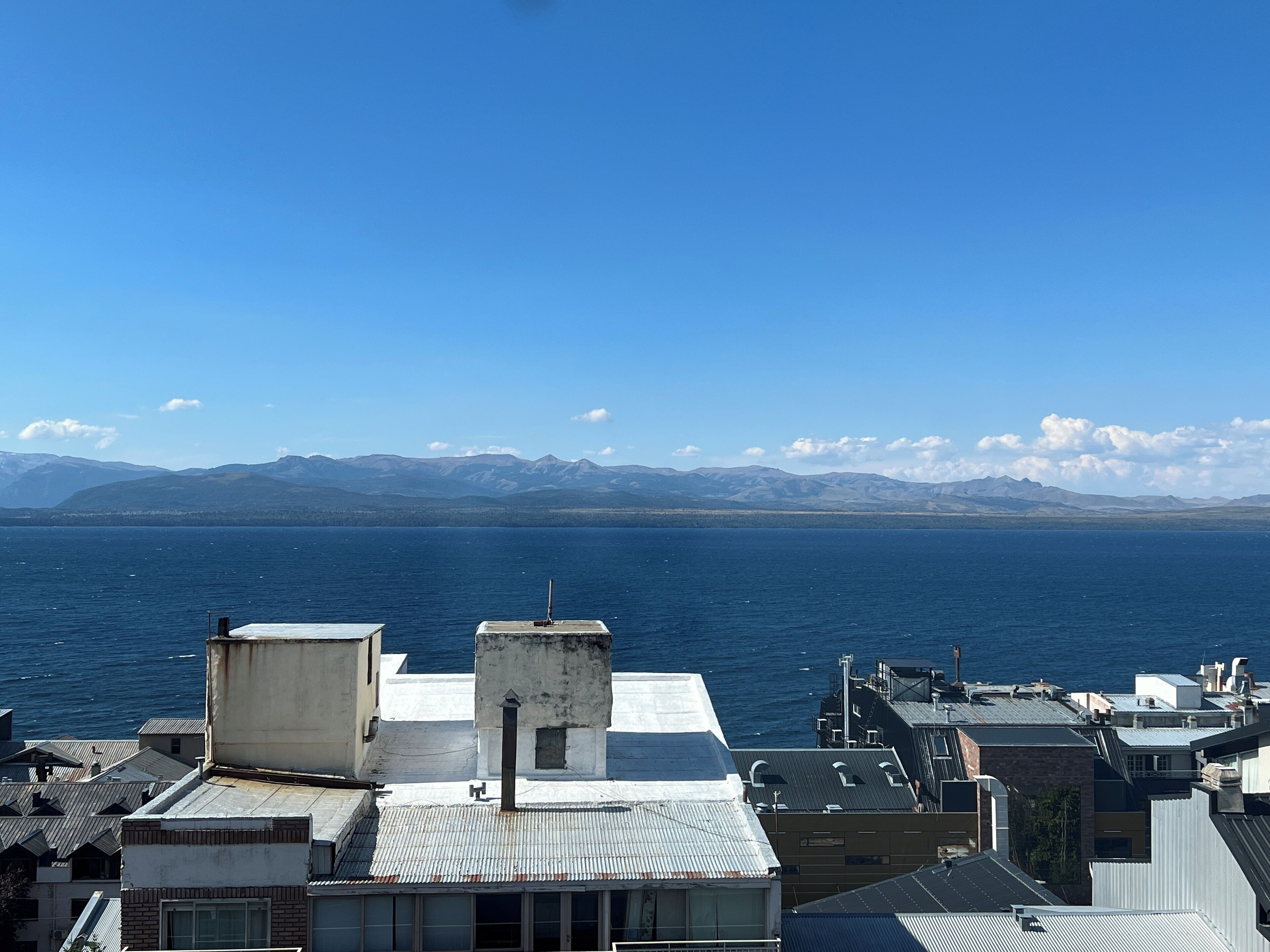 A coastal cityscape with buildings and a view of the sea and mountains.