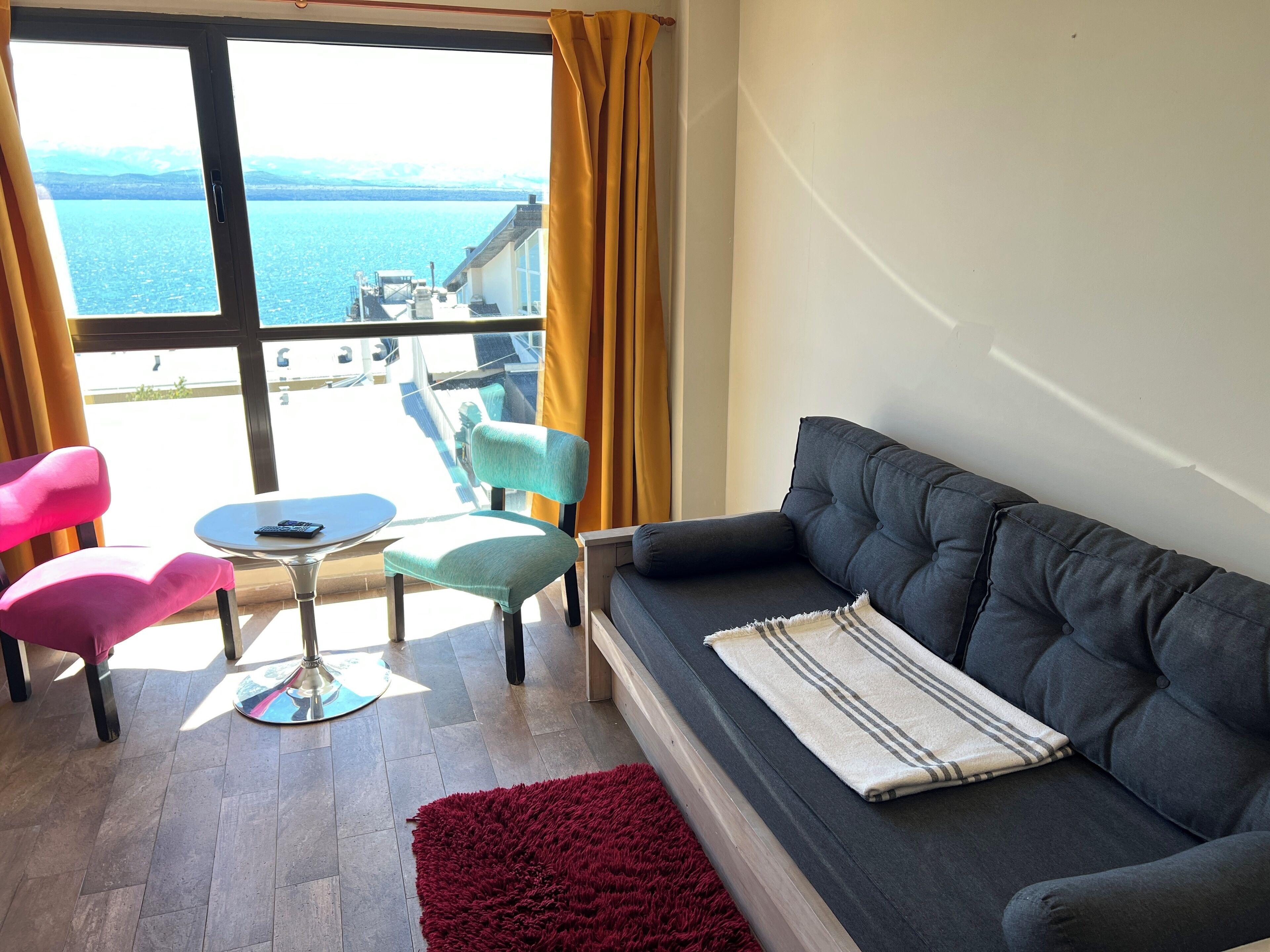 Un salon comprenant un canapé, deux fauteuils, une petite table et une vue sur une étendue d’eau, visible à travers de grandes fenêtres.