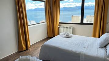 A hotel room with two beds, a view of the sea and mountains, and a radiator.