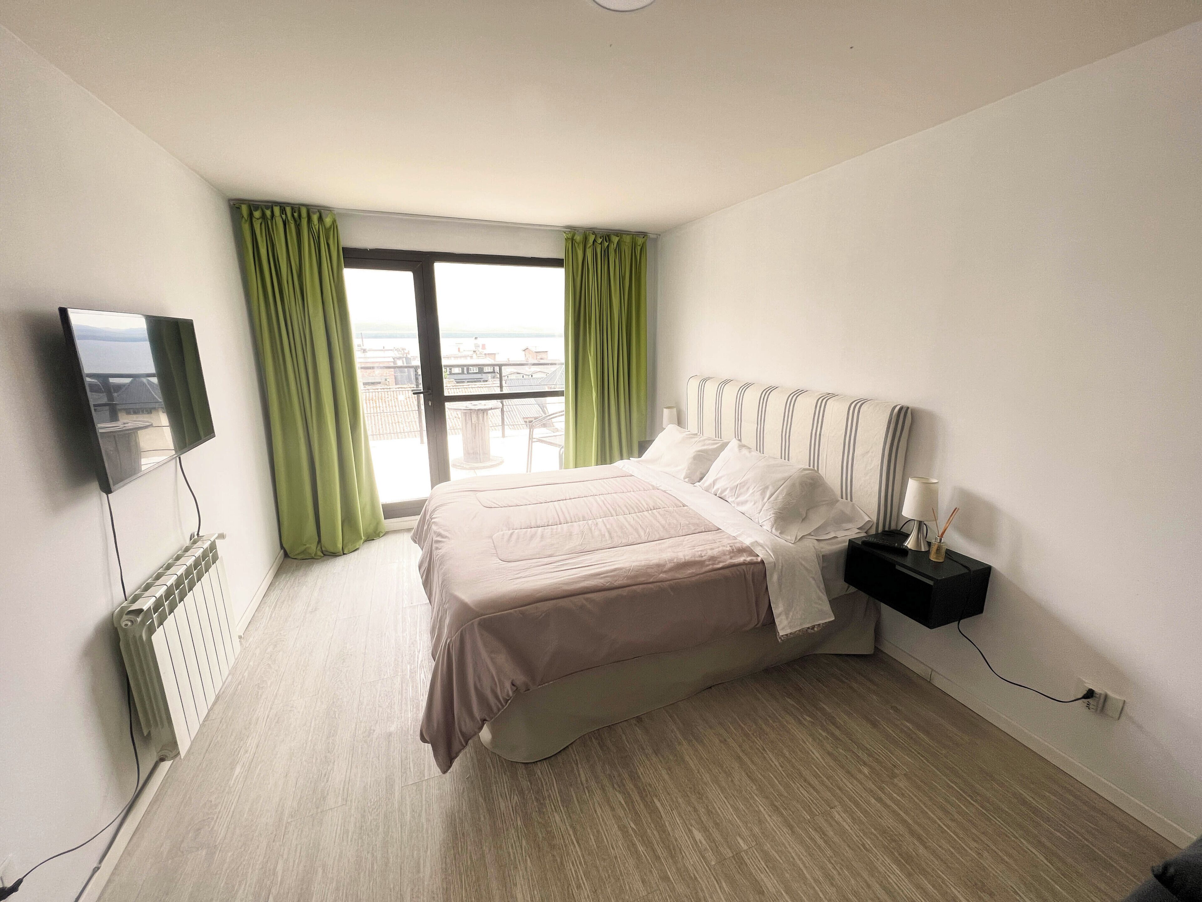 Habitación de hotel con cama, mesita de noche, televisor y ventana con cortinas.