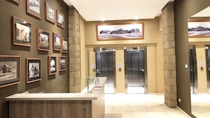 Un hall d’entrée avec des photographies encadrées accrochées aux murs, un comptoir d’accueil et deux ascenseurs.
