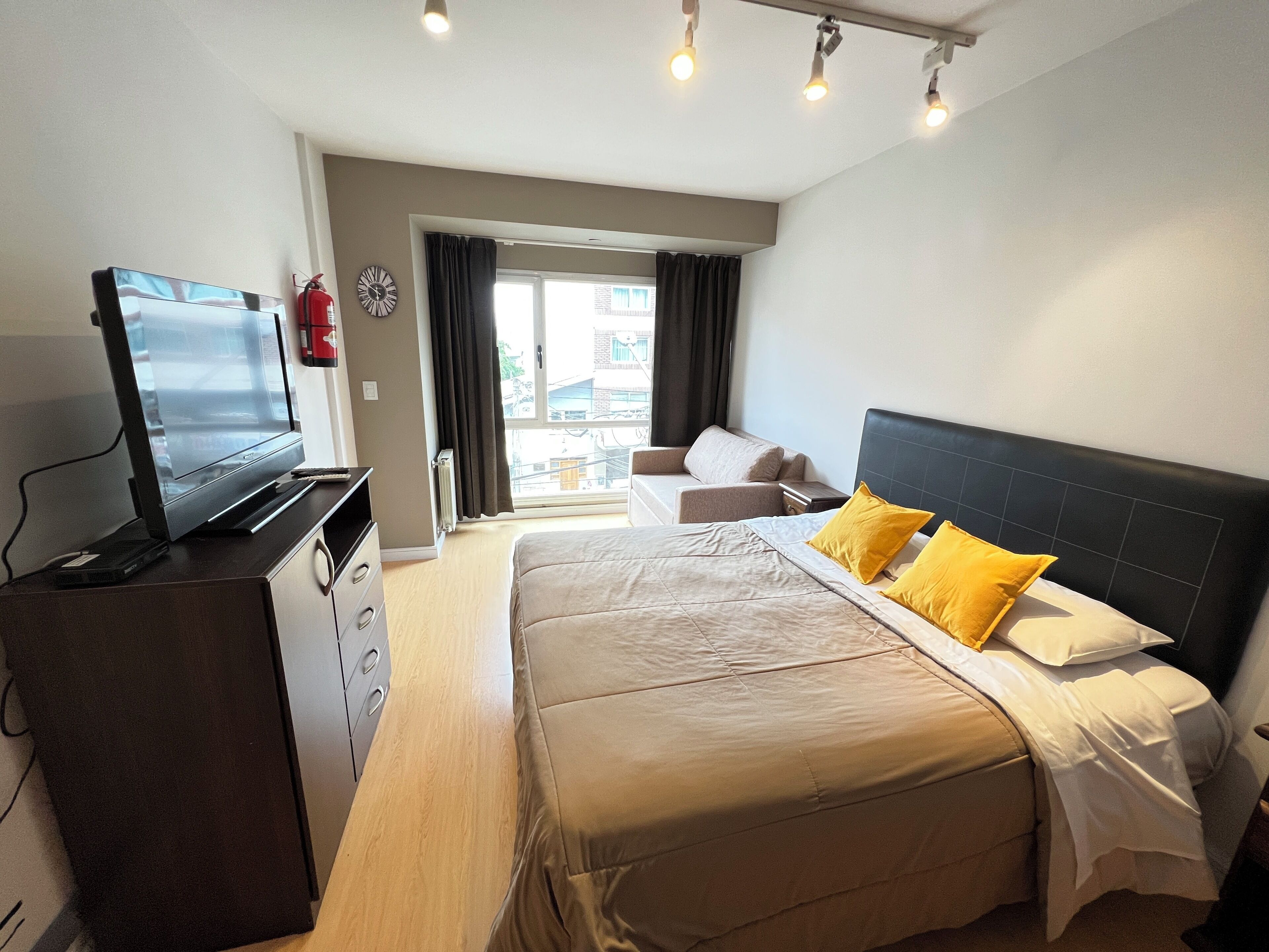 Une chambre d’hôtel avec un lit, un téléviseur posé sur une commode, une fenêtre avec des rideaux et une vue sur les bâtiments environnants.