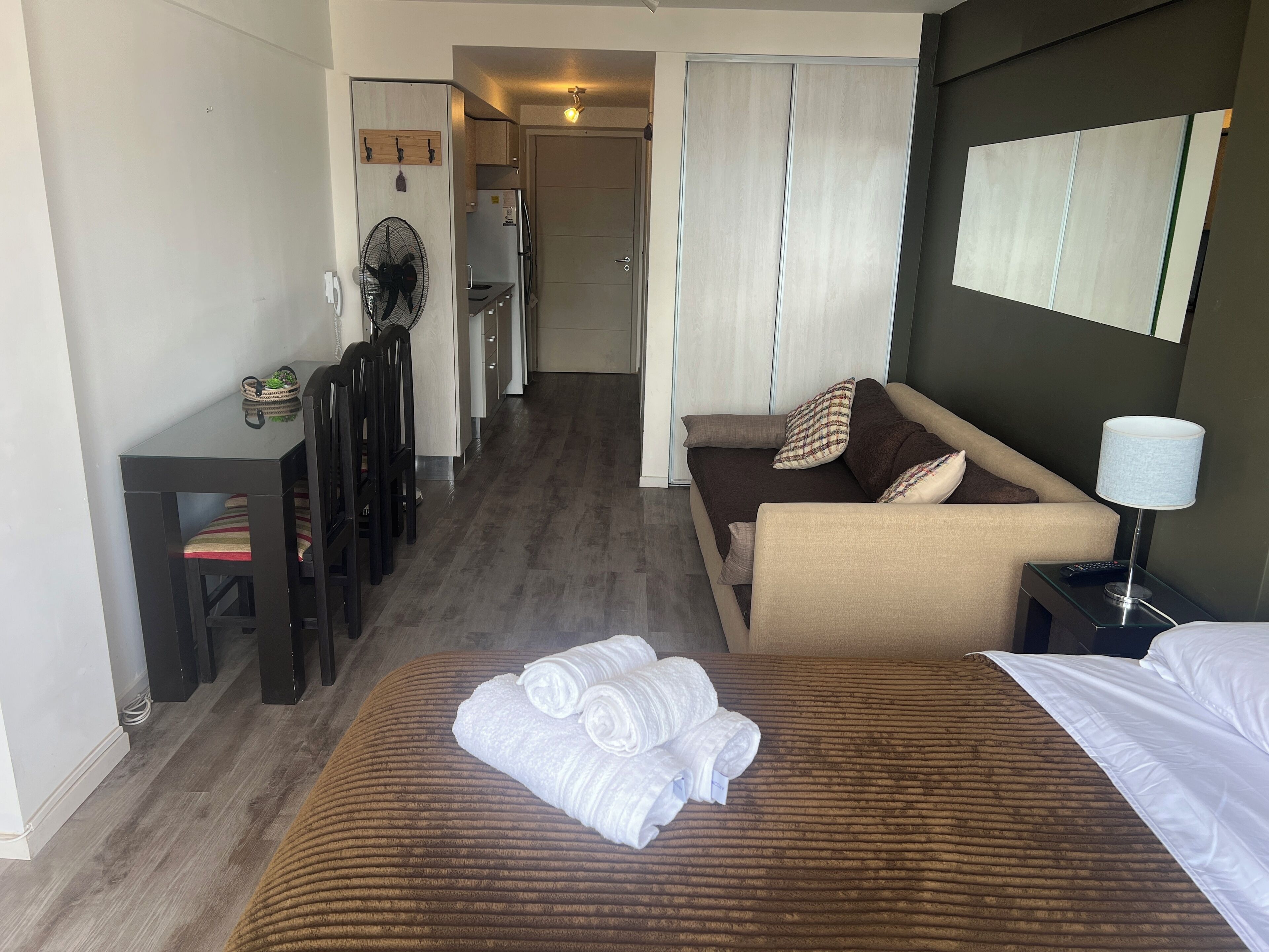 A hotel room with a bed, a sofa, a desk with chairs, a kitchenette, and a bathroom.