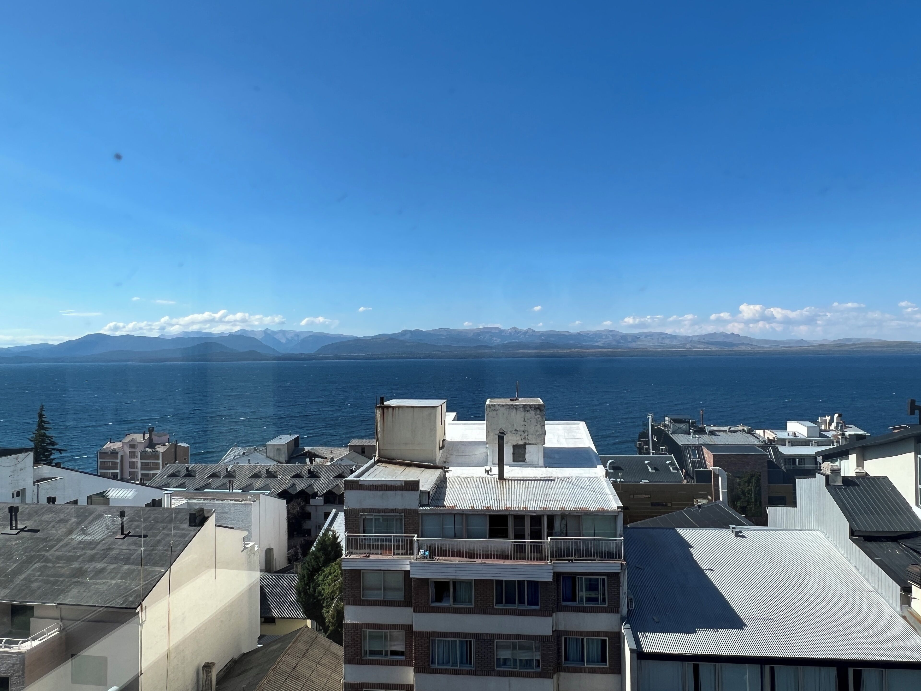 A high-rise building with multiple balconies overlooking a body of water and distant mountains.
