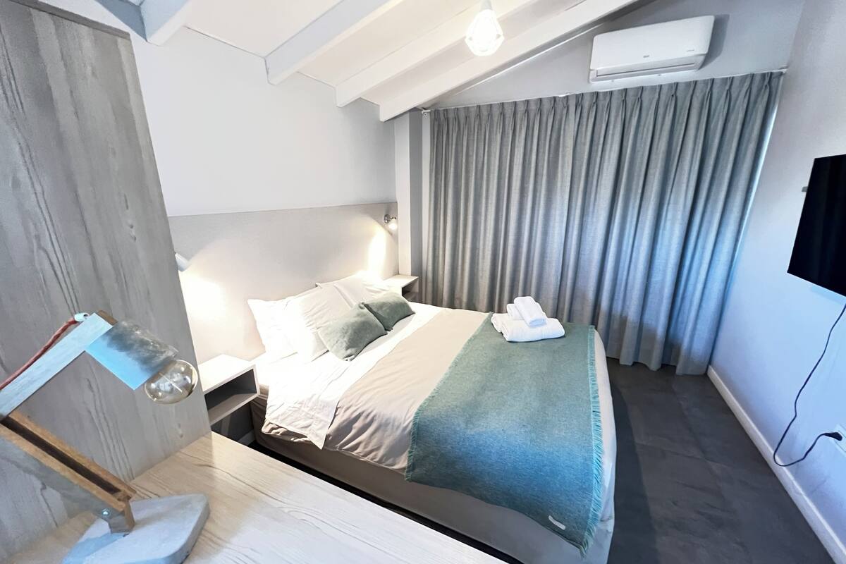 Habitació d'hotel moderna amb llit, escriptori, làmpada i finestra amb cortines.