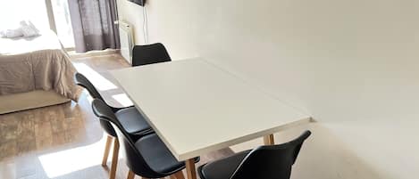 Ett modernt matområde med ett vitt bord och svarta stolar, en soffa och ett element.