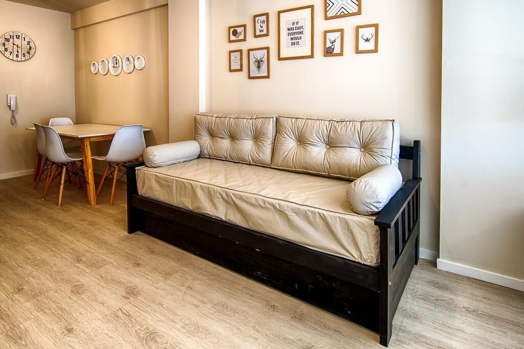 Una habitación con sofá cama, una mesa de comedor con sillas y un reloj de pared.