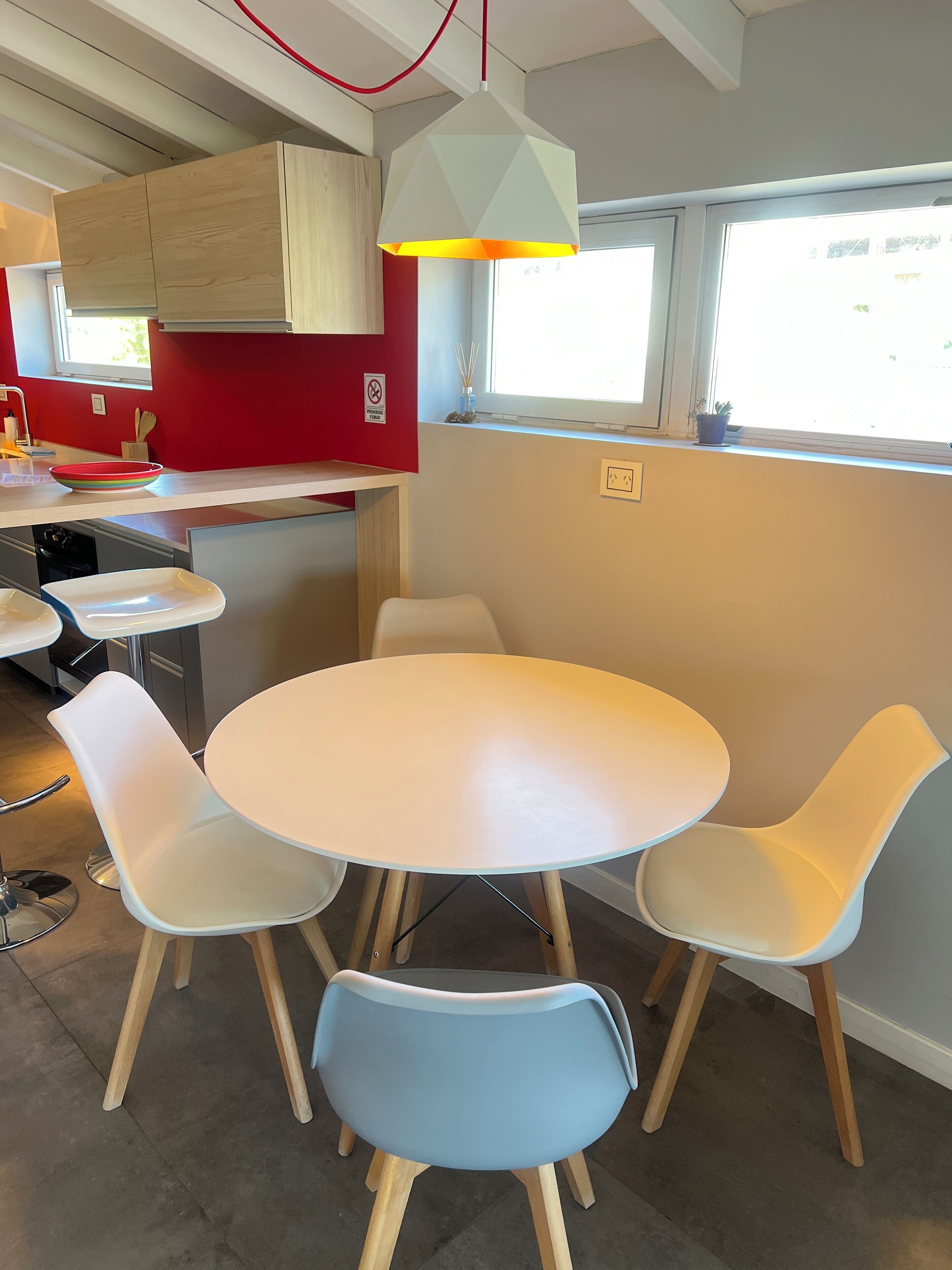 Een moderne keuken met een ronde eettafel en vier stoelen, een hanglamp en een raam met uitzicht.