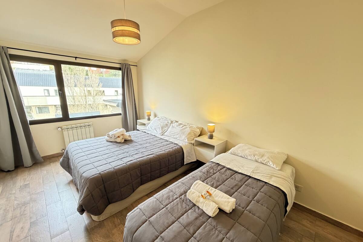 Habitació d'hotel amb dos llits, una finestra amb cortines, un radiador i una làmpada penjant.