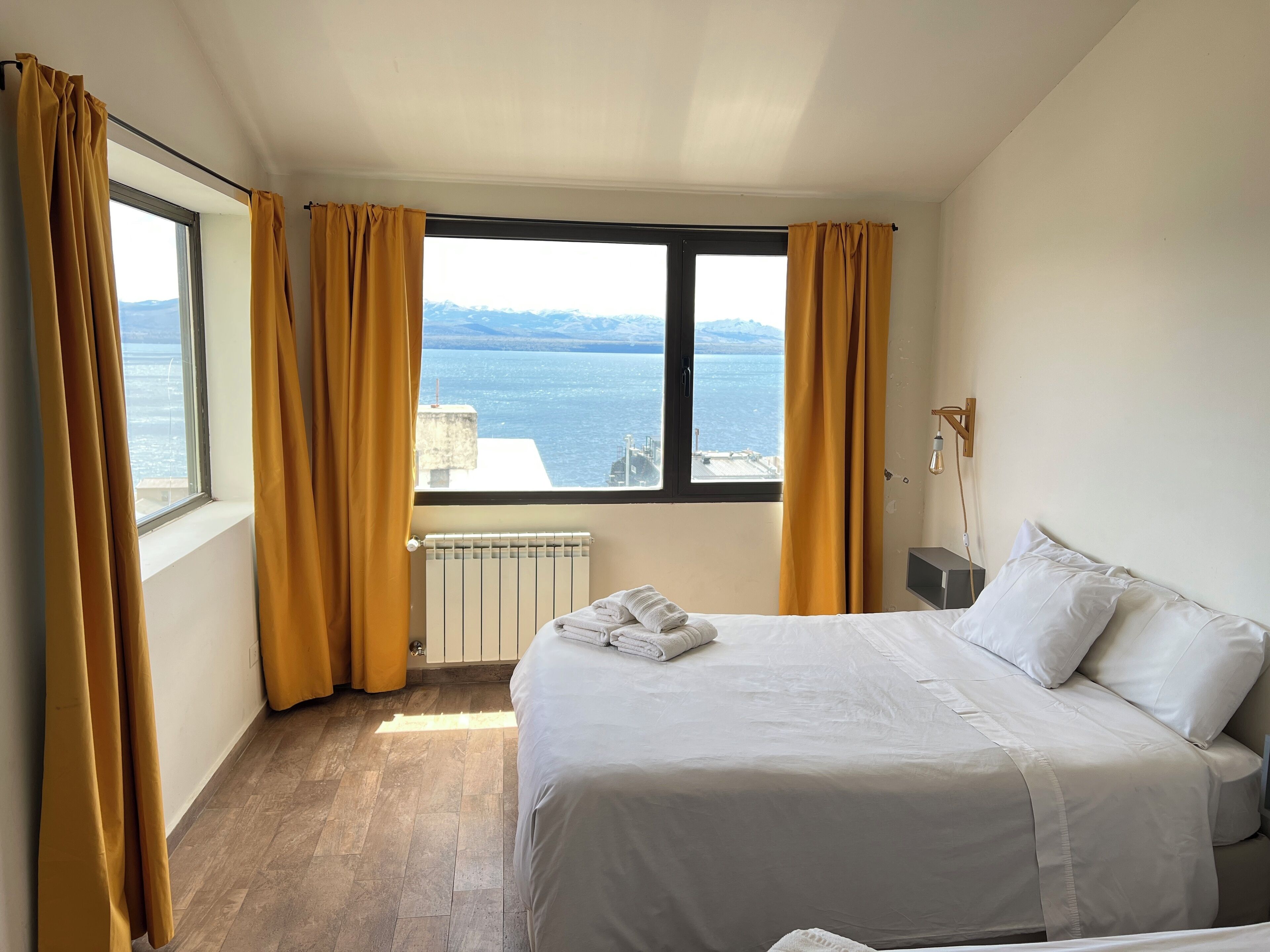 Ein Hotelzimmer mit Bett, Heizkörper, einem Fenster mit Vorhängen und Blick aufs Meer.