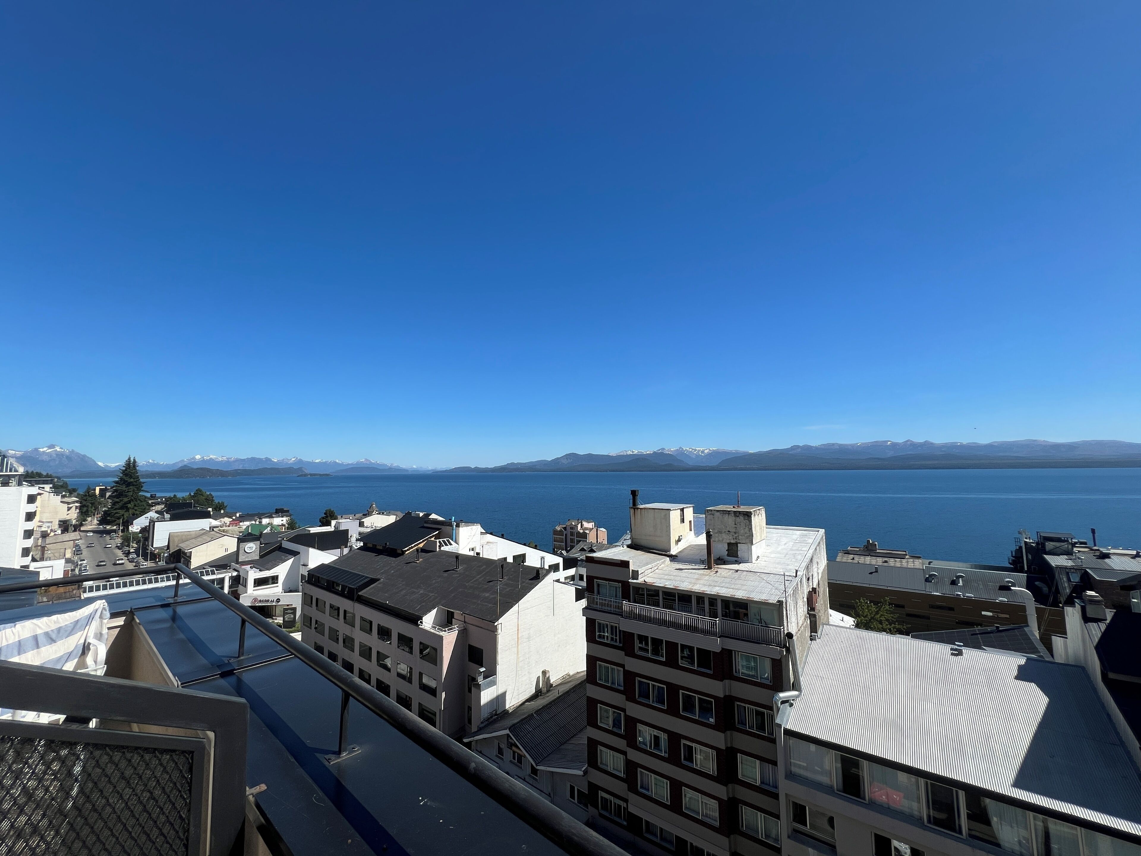 A cityscape with buildings and a clear view of a large body of water and distant mountains.