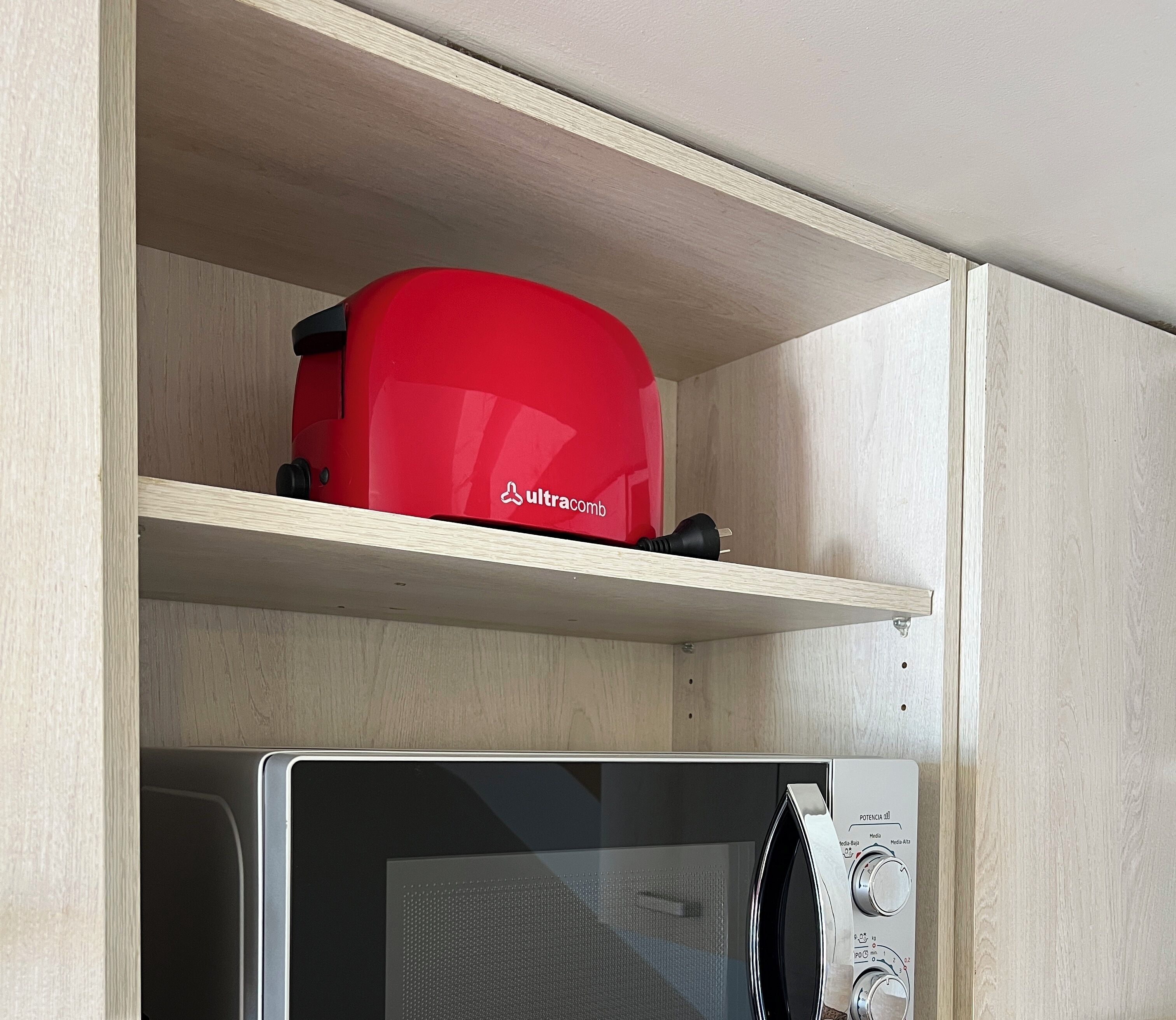 Uma cozinha com um micro-ondas e um eletrodoméstico vermelho numa prateleira.