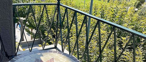 A balcony with a mosaic table, metal railing, and a view of buildings and trees.