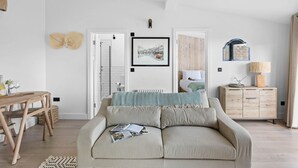 A modern bedroom with a large bed, a wooden dresser, a dining table, and a shower area. - The Sail Loft Suite - Sea View - Private patio (Brixham)